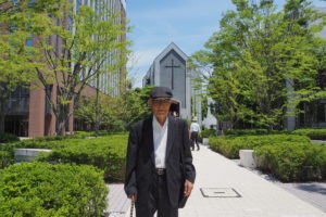 わたしの教会ストーリー　０１５　 大島(おおしま) 良雄(よしお) 師(し)（関東学院教会元協力牧師） 「平安のうちに感謝に満ちて過ごす日々」 私は東京で生まれ大阪北部の十三(じゅうそう)町に住まいました。その地にはバプテストの女子神学校とその付属施設の幼稚園、宣教師館、社会活動施設のミード社会(しゃかい)舘(かん)、淀川バプテスト教会がありました。その幼稚園に学び、卒園後は教会の土曜学校に通い、青年会に加わり、英語学校で学び、関西学院専門部、同大学というキリスト教的教育施設で育てられました。 【写真上】２０１７年、大学平潟祭の日曜日に大学チャペル前で 終戦後中国で宣教していたアメリカン・バプテストの宣教師が共産主義化した政府から圧迫され日本で活動するようになりましたが、活動を再開したミード社会舘にはミス・ウォーターマン（Miss Waterman）が来られ、私は会社の勤めが終わった後、彼女の自宅、YWCA、ミード社会舘で行われたバイブルクラス（Bible Class）で通訳として奉仕しました。戦火で消失した大阪淀川バプテスト教会が再建され、1949年の秋アキスリング博士（Dr.Axling）の伝道集会が催された時に入信しました。意識的に信仰を告白する機会となる集会は信仰生活に欠かせない決断の時でしょう。使用されたテキストはフィリピの信徒への手紙4章10～14節で、強調されたのは13節でした。この集会は自分の信仰を見直し、確認する時になりました。 やがて私は勤務先の仕事に飽き足らず社会福祉関係の仕事に関心を持ち、午前中は関西学院大学で社会福祉学を聴講し、午後から会社で働く苦学生になりました。それを知ったMiss Watermanは母教会の牧師と相談し米国の神学校に学ぶ道を開いてくれ、神学校卒業後、社会福祉を学ぶことにして留学しました。バークレー・バプテスト神学校を卒業した時、学校経営上の問題で院長排斥運動をしていた尚絅女(しょうけいじょ)学院(がくいん)の院長から同校に就任するよう再三要請され皮肉なことに最も避けたかった牧師と教師の仕事、しかも両者を兼務する仕事に就きました。紛争問題に関わることは避けて職務に忠実であるよう努力しました。ある時高校3年のクラスの担任が突然来宅され、クラスの信仰調査の結果大半の生徒が信徒になっているのを知った、と報告され敬意を表してくれました。個人的に関心のあった社会事業も研究に努め、短大で社会福祉各論の授業も担当しました。 短大と中高チャプレン（学校や施設で働く聖職者）と教師とを兼任の仕事にも慣れた頃、関東学院大学白山(しらやま)学長から大学宗教主任としての招聘状が届きました。当時大学のチャプレンとして素晴らしい活動をしていたジェニンス博士(Dr.Jennings)が 突然帰国したのでチャプレンが不在になり、後任として私が招かれました。白山大学長の招聘の辞には「学院の定款(ていかん)に、宗教主任をおくとあるので招聘したいが、給与規定がないので無償の働きとなる。生活の資は大学の教員としての俸給をもって充てて欲しい」というものでした。乞われれば辞さない性格のためか安定した仙台での生活を捨てて横浜での冒険的な生活を始めました。チャプレンの仕事には規定がなく、大学の宗教的行事，特に外部の施設を借りて行う入学式、卒業式、クリスマス、その他の行事のための横浜市や進駐軍の施設の借用、式典の執行、学内の毎朝の礼拝の諸準備、特別 【写真左】２０１７年１２月、関東学院教会主日礼拝での説教 講演会のための講師の依頼、実施、天城山荘（キリスト教の宿泊・研修施設）での教職員の修養会の準備及び実施などのほか学院の諸学校の聖書研究会、YMCA、 大学青雲寮(せいうんりょう)の行事の援助、学生の指導、「告知板」，キリスト教報の発行、大学敷地内にあった事業部メッキ工場（現在の関東化成工業株式会社）での説教、日本バプテスト同盟の外国人の来客の空港への送り迎えと滞在中の接待などで、文字通り多忙を極めました。多忙な仕事を無事に果たせたのは主の憐れによるものと感謝しています。 【写真上】２０１９年５月、主日礼拝後、大学キャンパス中庭で 最後に近況を報告したいと思います。100才を超えた頃から心身の機能の劣化を感じる様になりましたが、街を走る自動車が年月の経過と共にその機能が劣化するのを見て、自分の身体の機能の劣化も自然現象として受容していました。ある日突然精神面の劣化を覚え、信仰の劣化について懸念するようなりました。聖書に解答を求めました。ある日普段は余り読んで居なかったソロモンの教えであると言われる「コヘレトの言葉」を読んでいた時、答を見出しました。人間の生死は神のみが係わる事で、すべての時は神の定めによる。我々に必要な事はその定めを信じることである、と言うのです。コヘレトは、全ての事に時があると述べています。全てを支配される神に全てをゆだねる信仰によって平安のうちに感謝に満ちた日々を過ごしています。 　　 アーメン 【写真上】２０２３年１１月、ご自宅にて 